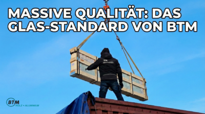 "Ein BTM-Montageteam entlädt mit einem Kran massives Sicherheitsglas für hochwertige Holz-Alu-Fenster vor blauem Himmel."